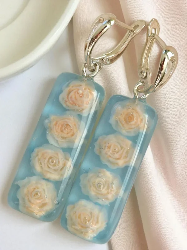IzArtShop resin oorbellen met lichtblauwe tint en klei roosjes. Handgemaakt, 5 cm lang met RVS oorhangers. Licht, elegant en uniek sieraad.